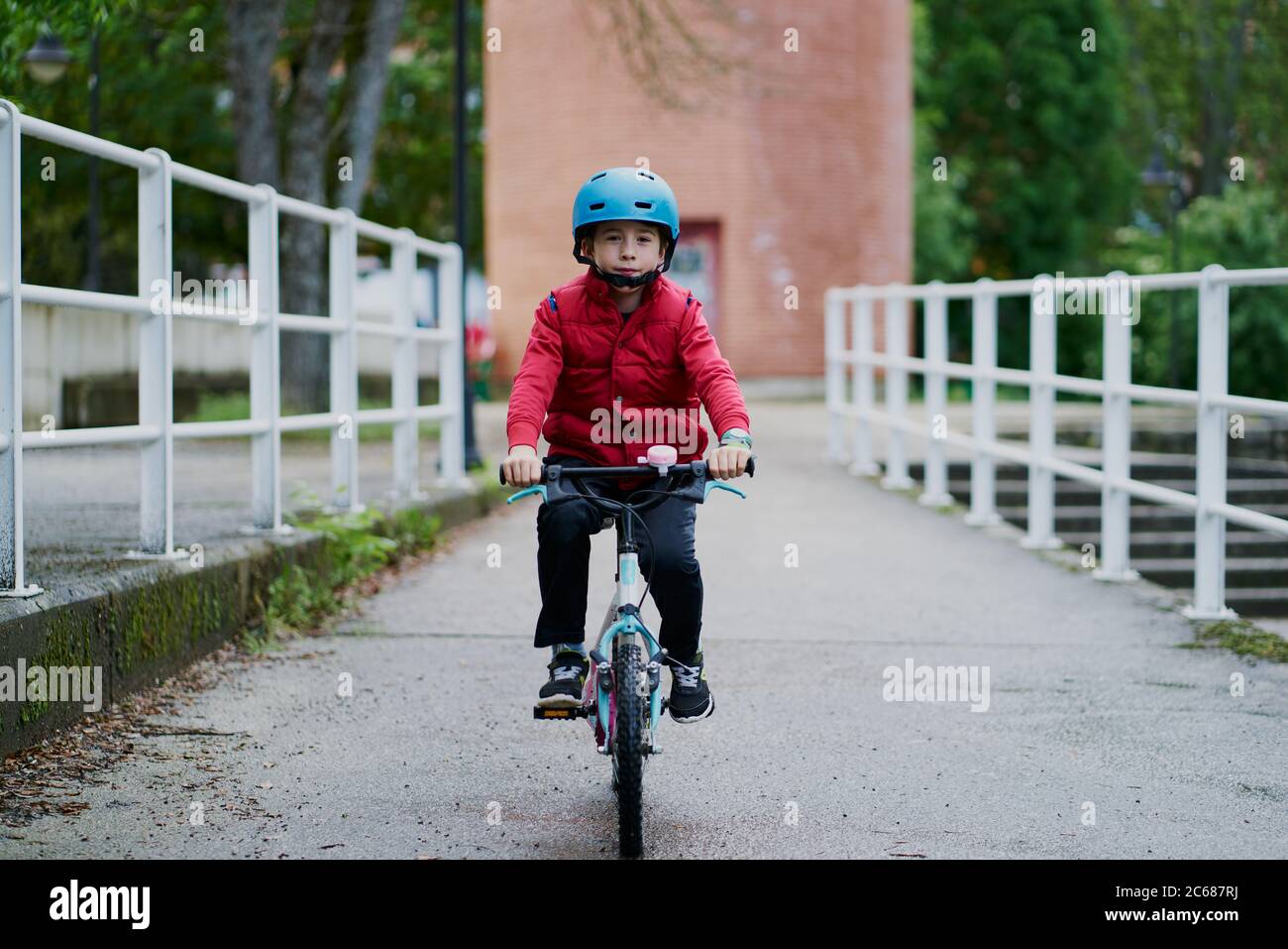 ragazzo che cavalcava una bicicletta con un casco blu e un soprabito rosso Foto Stock