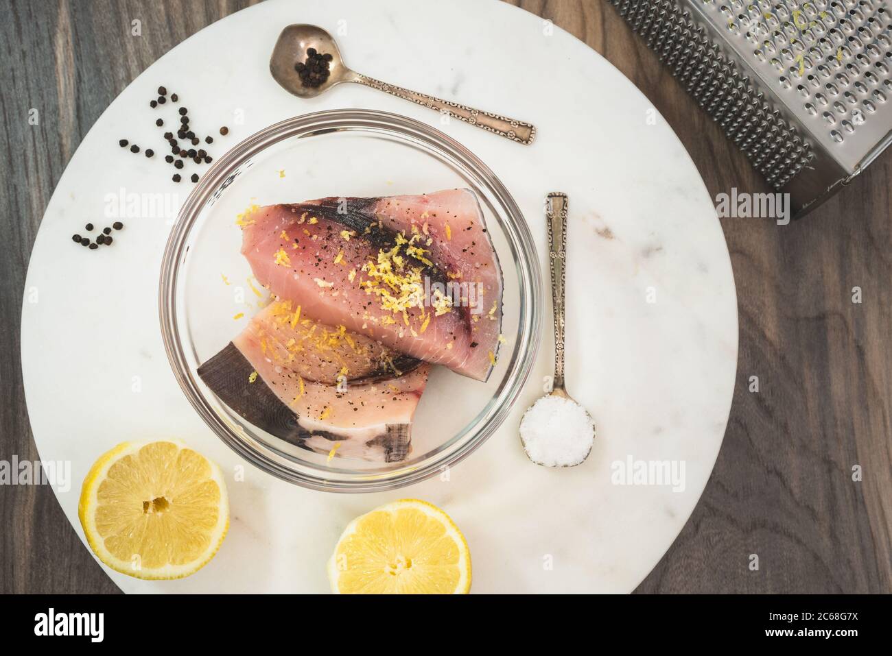 Pesce spada crudo marinato con sale, pepe nero e scorza di limone. Due pezzi di bistecche di pesce fresco crudo in una ciotola su un tagliere di marmo con alcuni incartati Foto Stock