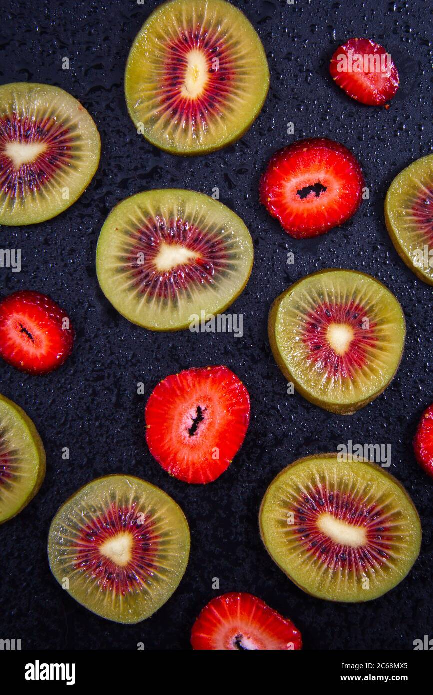 Vista ravvicinata di minuscoli frutti, kiwi verdi e rossi e una fragola matura rossa. Foto Stock