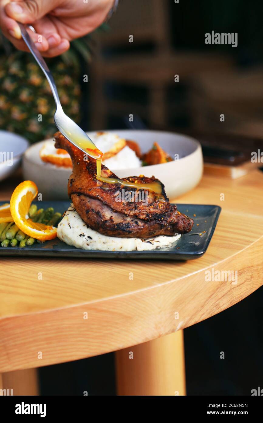 bastone di pollo arrosto con salsa di mandarino su purè di patate su piatto nero su tavolo di legno Foto Stock