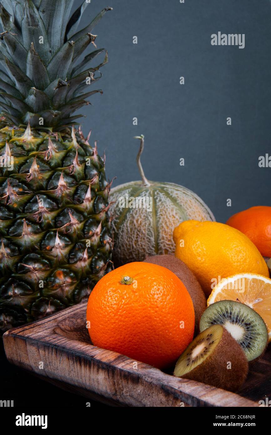 Una ciotola di legno piena di kiwi verdi, arance e limoni vicino ad un melone di miele, una mela di pino e una lanterna cinese su uno sfondo nero. Foto Stock