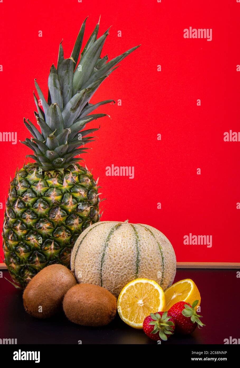 Un melone di melone, un ananas, e arancio, limoni, kiwi, fichi di barbaro e lanterne cinesi davanti ad una parete rossa. Foto Stock