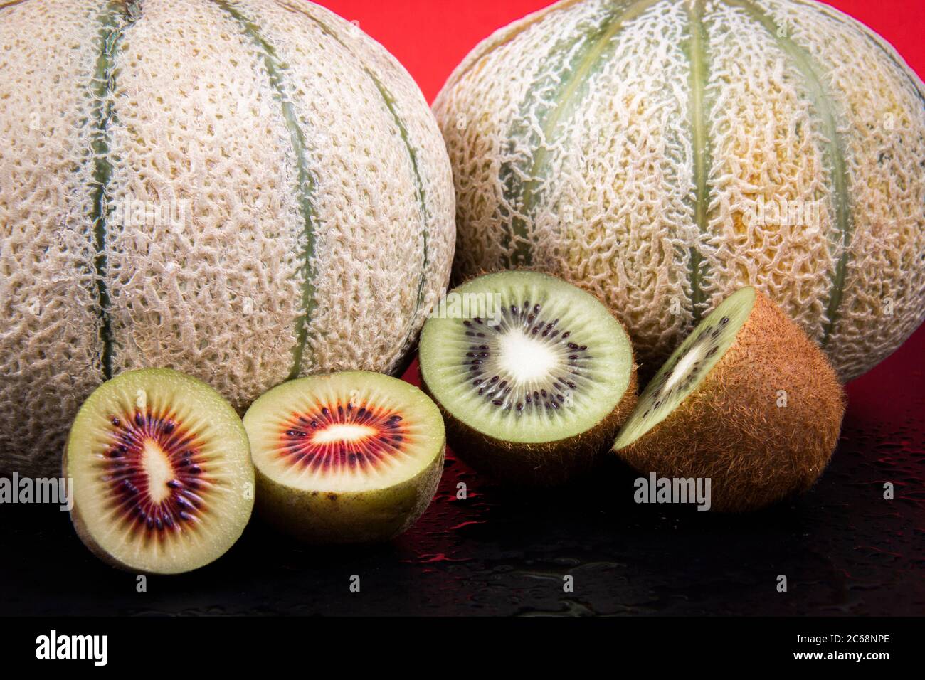 Due meloni pieni di melone e due kiwi dimezzati, un kiwi verde e uno rosso. Foto Stock