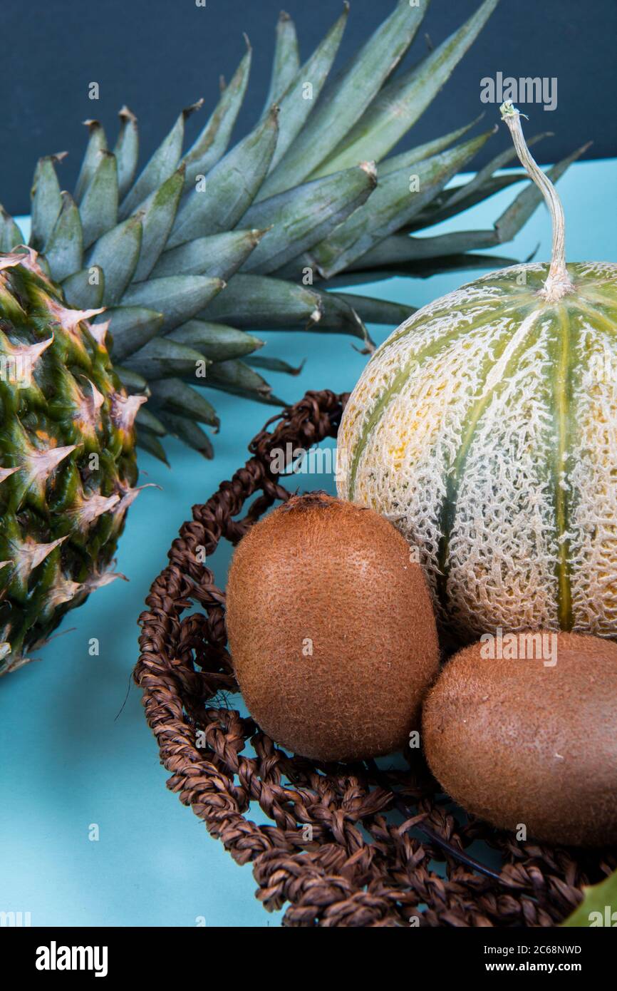 Una ciotola di kiwi pieno e dimezzato e una melone di melone di miele vicino alle foglie di un ananas. Foto Stock
