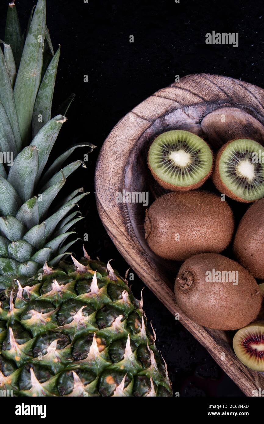 Una ciotola di kiwi pieno e dimezzato e una melone di melone di miele vicino alle foglie di un ananas. Foto Stock