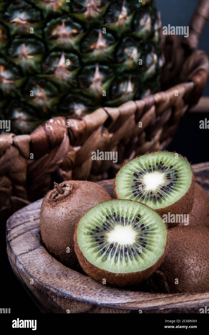 Una ciotola di kiwi pieno e dimezzato e una melone di melone di miele vicino alle foglie di un ananas. Foto Stock