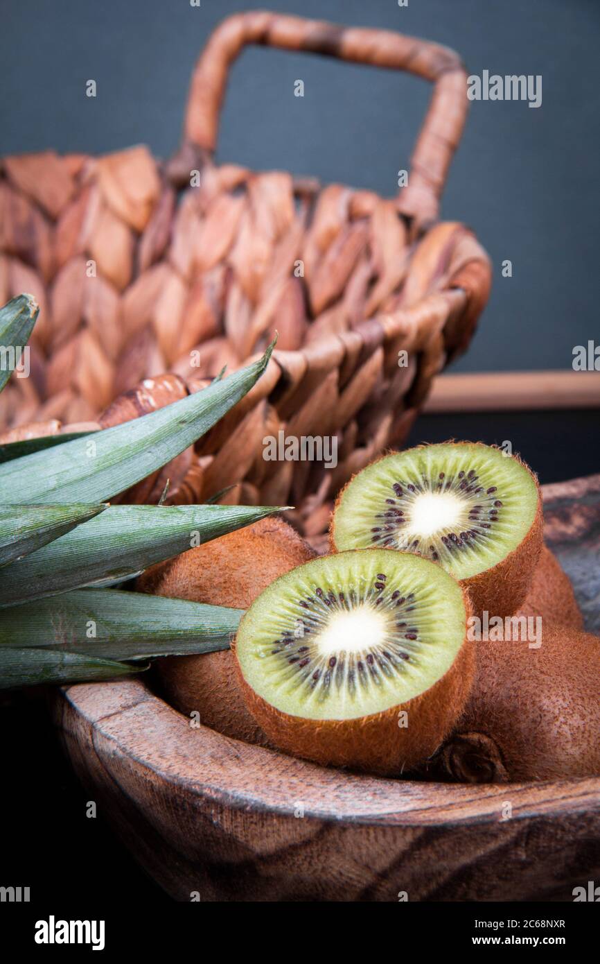 Una ciotola di kiwi pieno e dimezzato e una melone di melone di miele vicino alle foglie di un ananas. Foto Stock