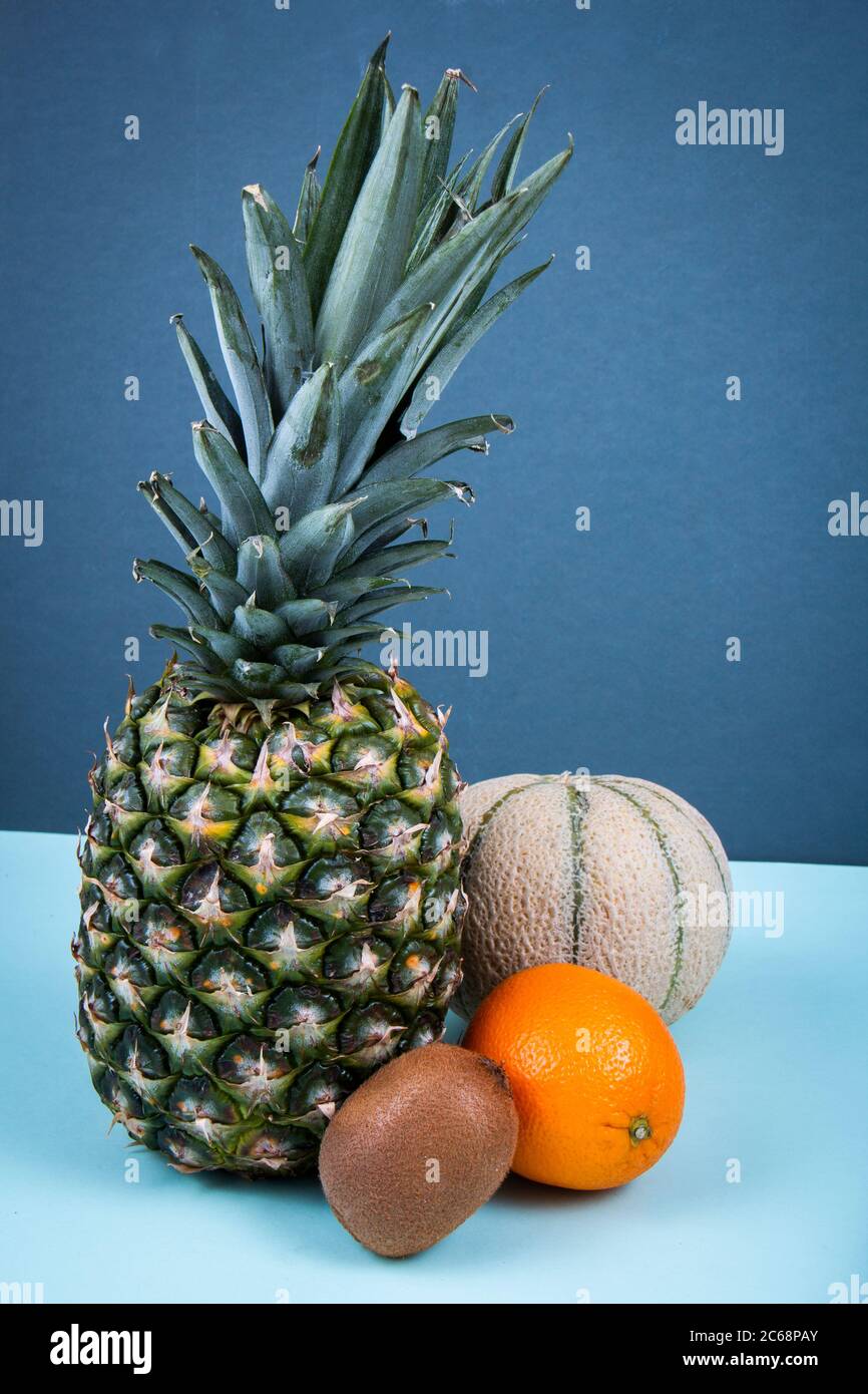 Un ananas, melone di melone, arancio e kiwi su una superficie blu. Foto Stock