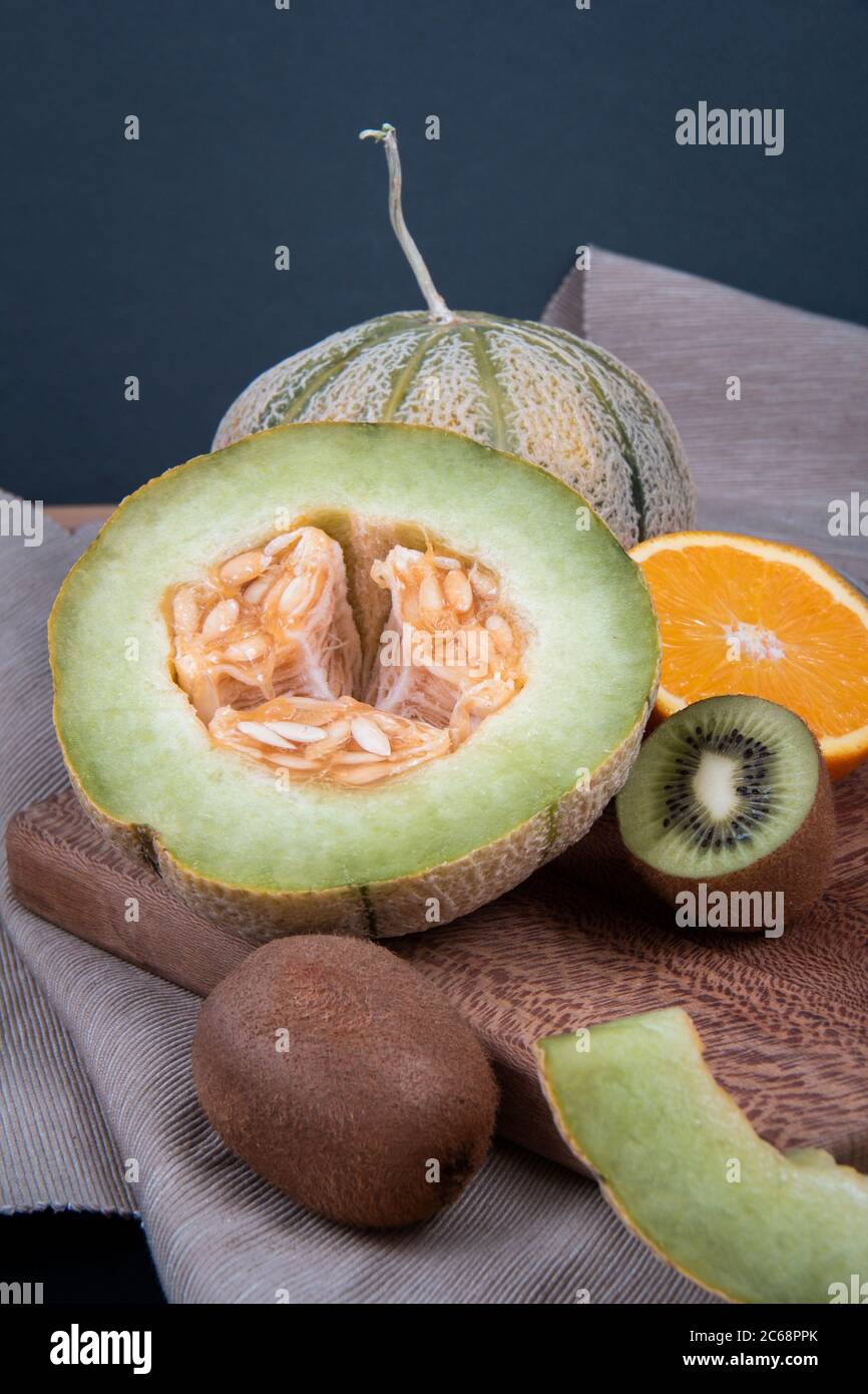 Meloni di melone, kiwi tritati e metà di un arancio dolce su un pannello di legno. Foto Stock