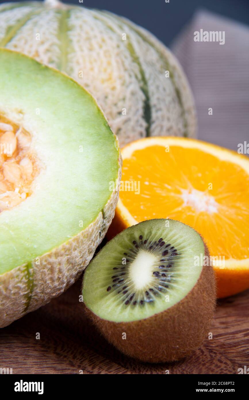 Meloni di melone, kiwi tritati e metà di un arancio dolce su un pannello di legno. Foto Stock