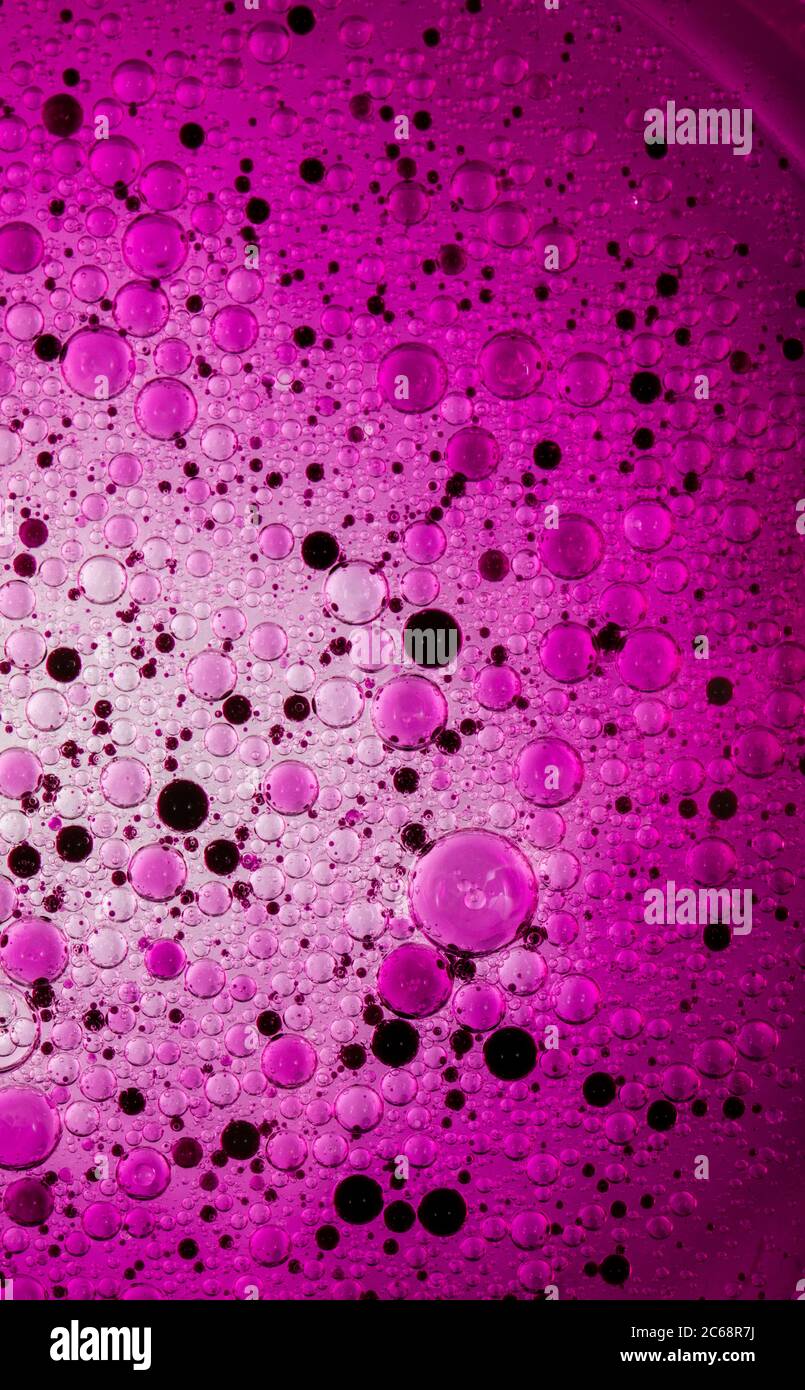 Bolle d'olio nell'acqua. Colori rosa e viola e nero. Foto Stock