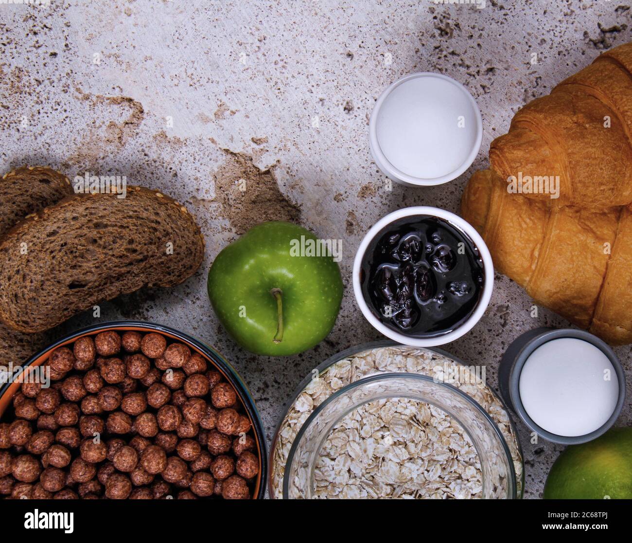 Un perfetto tavolo per la colazione pieno di frutta fresca: mela e arancia, diversi tipi di pane: Croissant e pane tostato, marmellata, bastoncini salati, avena e capretto Foto Stock