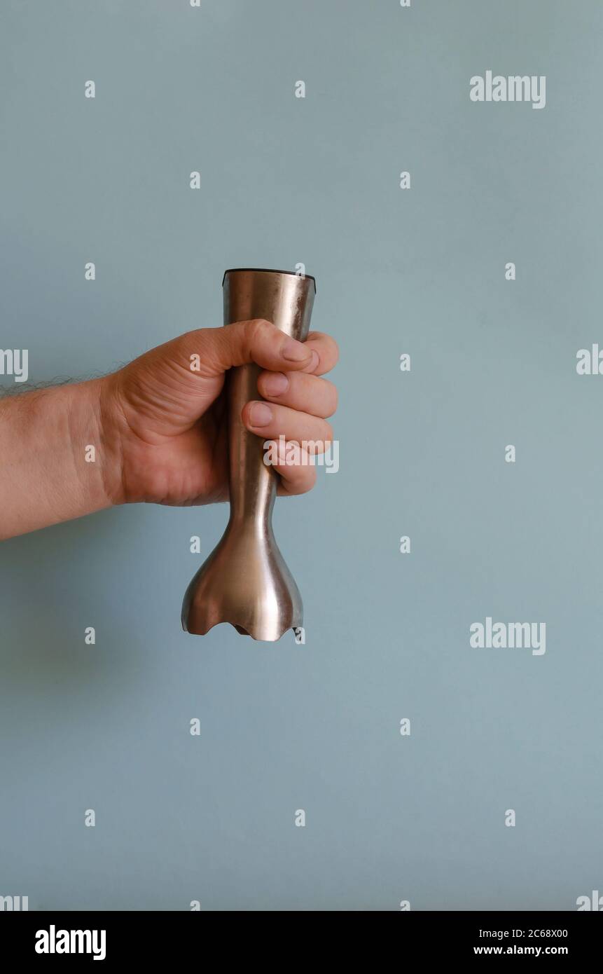 Porta-accessori per mixer da cucina. La mano sinistra di un uomo con un attrezzo metallico con coltelli speciali. Uomo caucasico 43-45 anni. Cucina Foto Stock