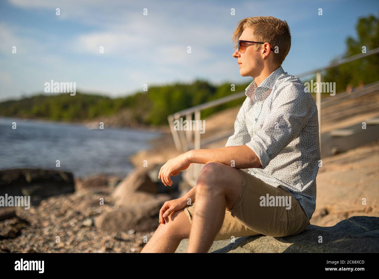 Pensieroso giovane uomo seduto su roccia guardando al mare Foto Stock