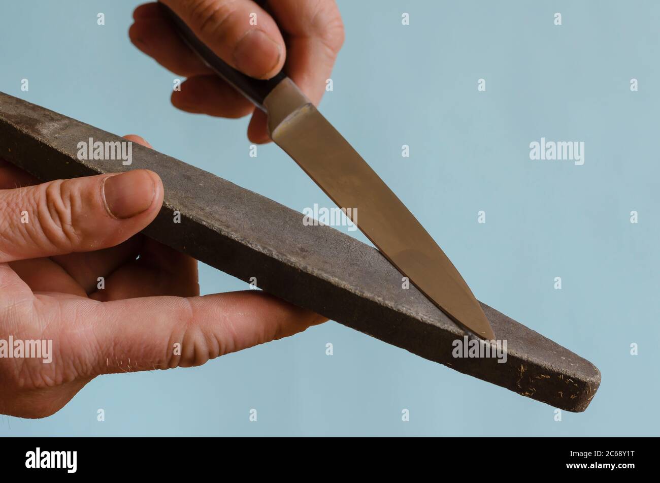 Le mani dell'uomo stanno affilando un coltello piccolo su una mola. Il processo di rettifica manuale di un utensile da taglio. Uomo di razza europea di mezza età. Anche la mano Foto Stock