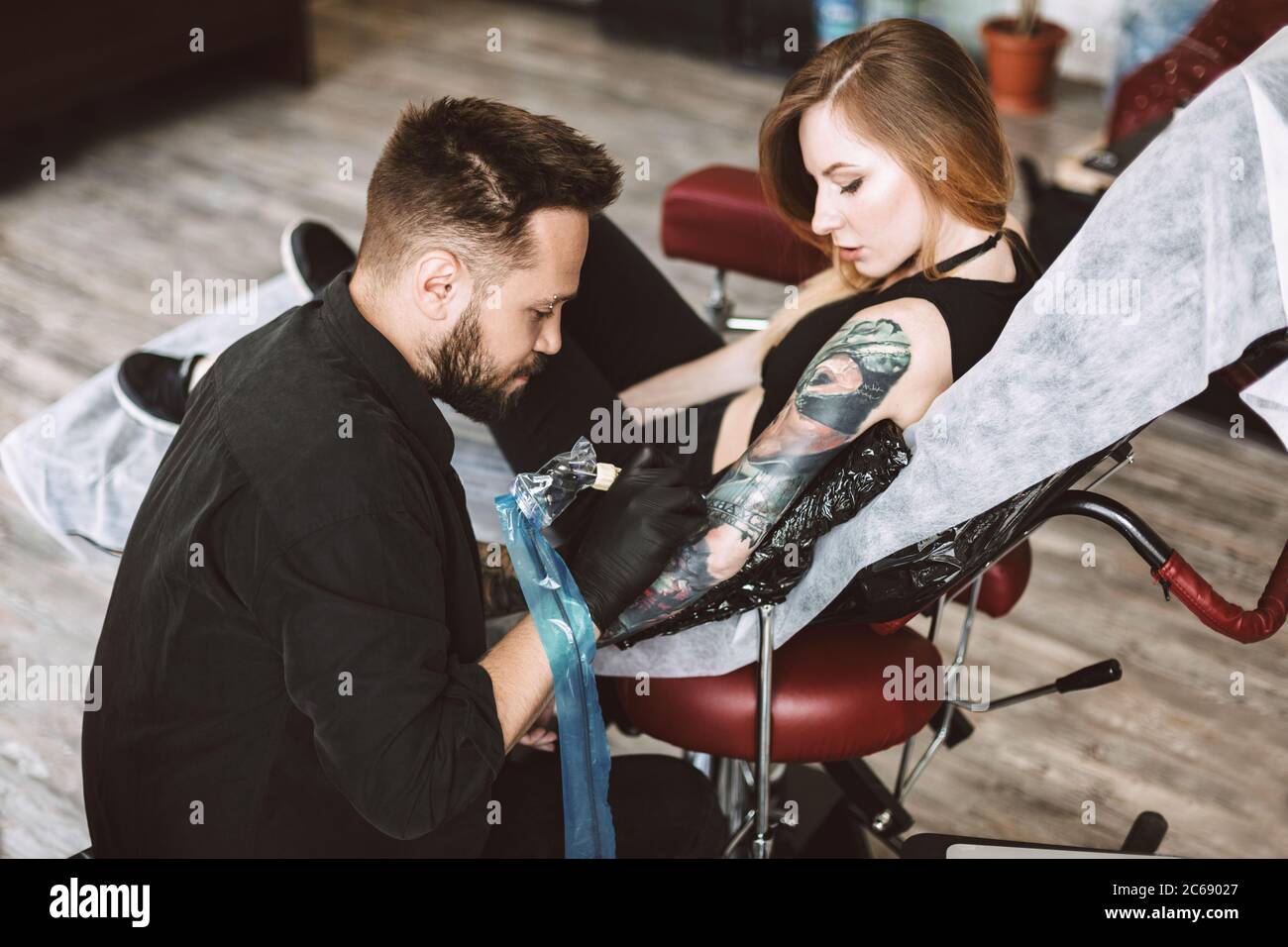 Tatuatore professionale che fa tatuaggio a mano da macchina tatuatrice mentre la ragazza guarda attentamente processo in studio Foto Stock