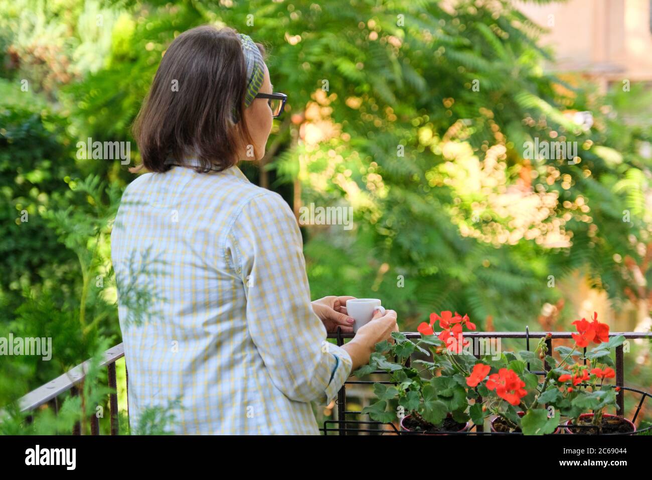 Ritratto di donna di mezza età che si rilassa sul balcone paesaggistico con una tazza di caffè Foto Stock
