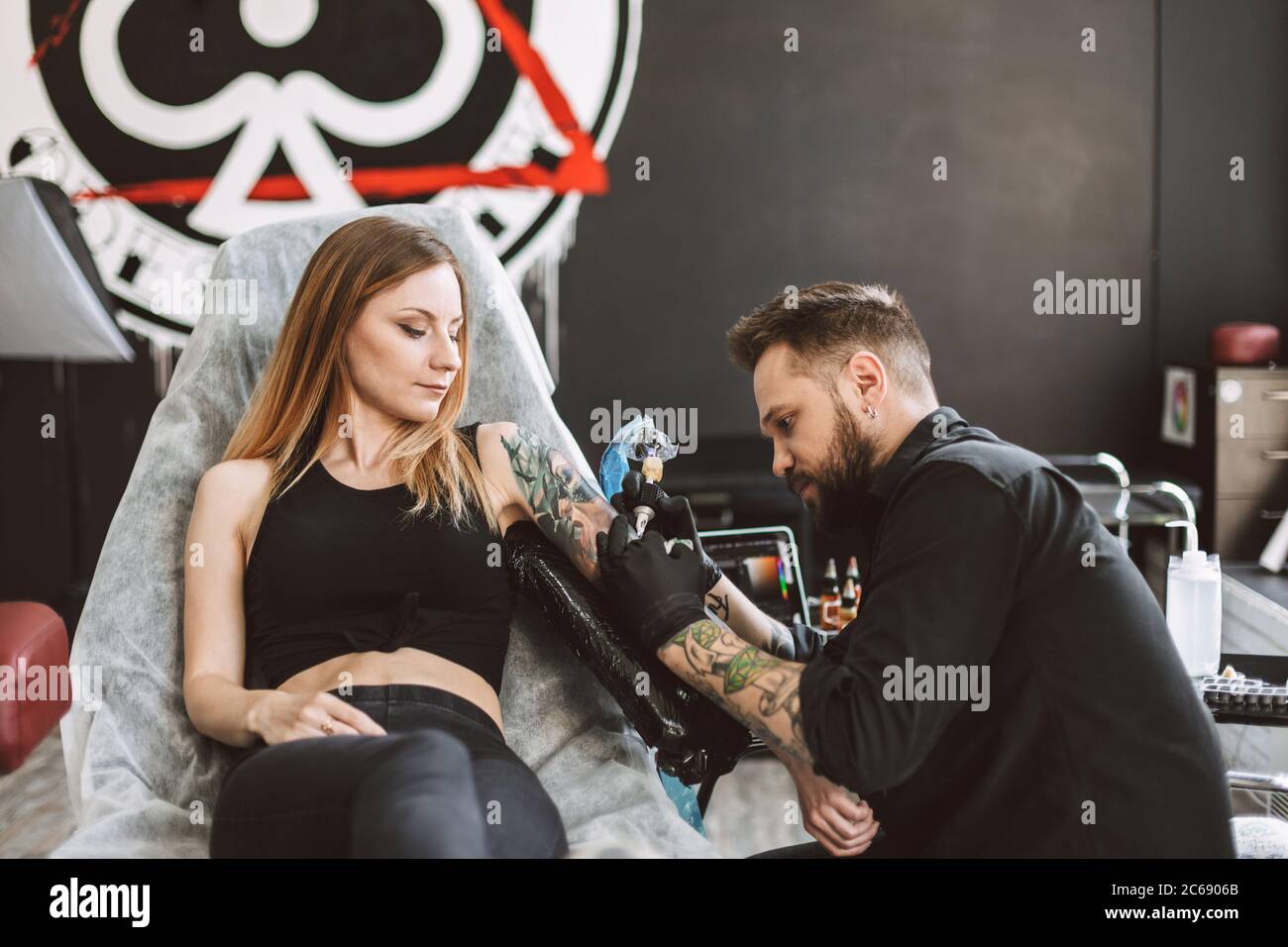 Tatuatore professionale che fa tatuaggio sulla mano della ragazza usando la macchina del tatuaggio in studio moderno Foto Stock