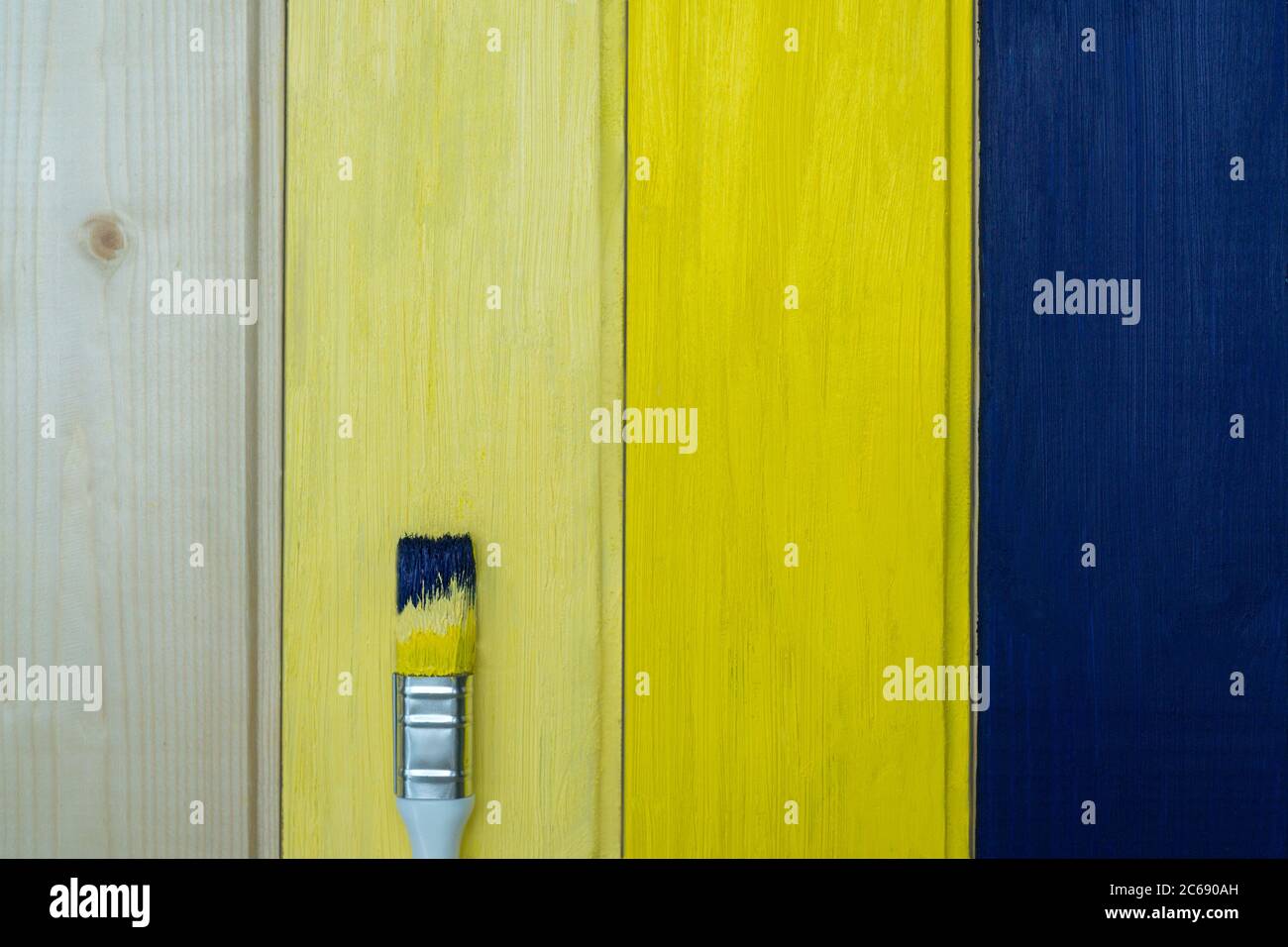 Il pannello è dipinto di blu e giallo e un pennello con vernice blu giallo su sfondo di legno. Blu - colore dell'anno 2020. Migliore combinazione c Foto Stock