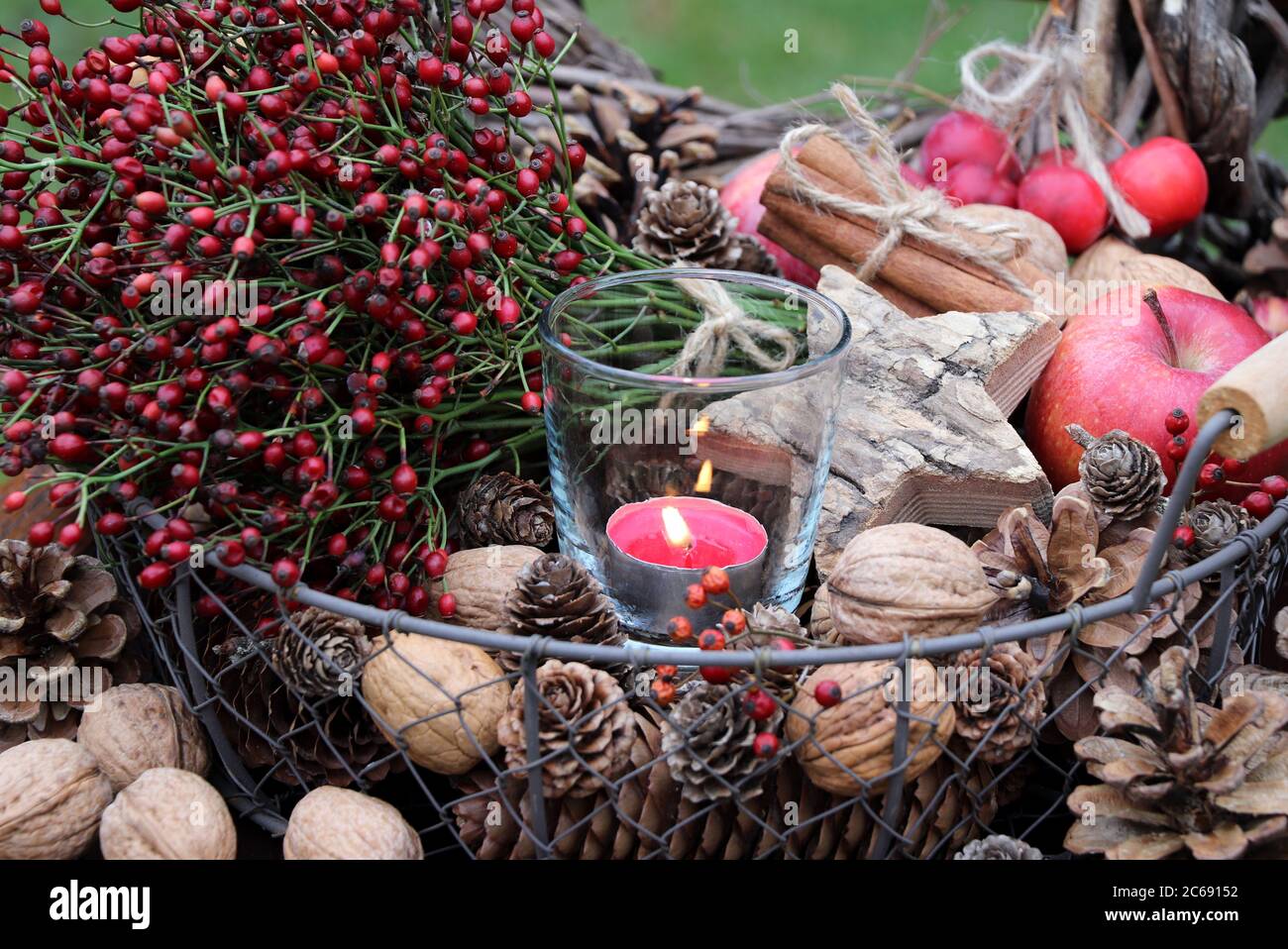 cesto con rose, noci, mela, stella di legno e candela come decorazione invernale Foto Stock