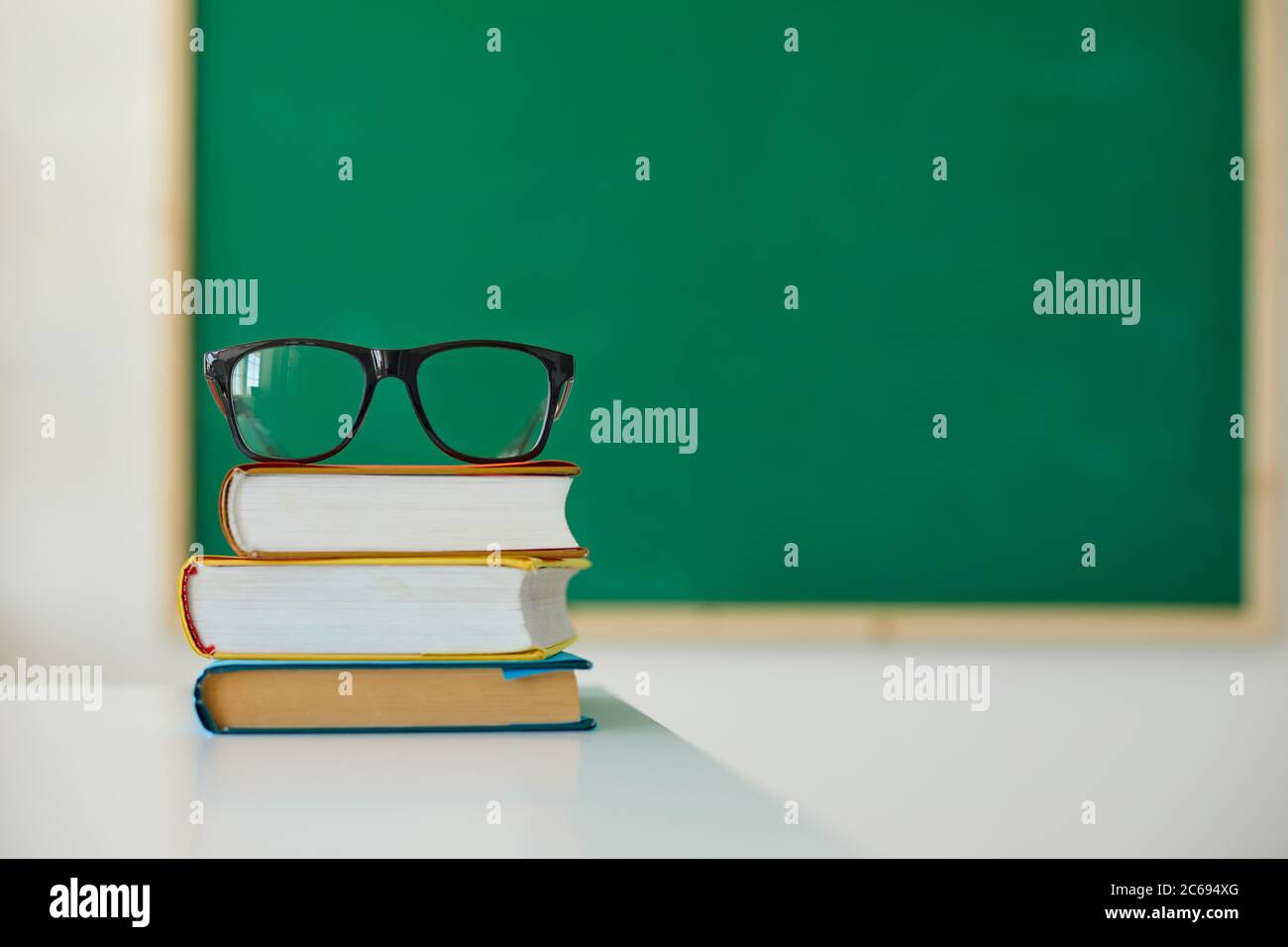 Istruzione scolastica. Stack di libri e bicchieri per insegnanti sulla scrivania in classe. Mucchio di libri di testo di copertina rigida sul tavolo Foto Stock