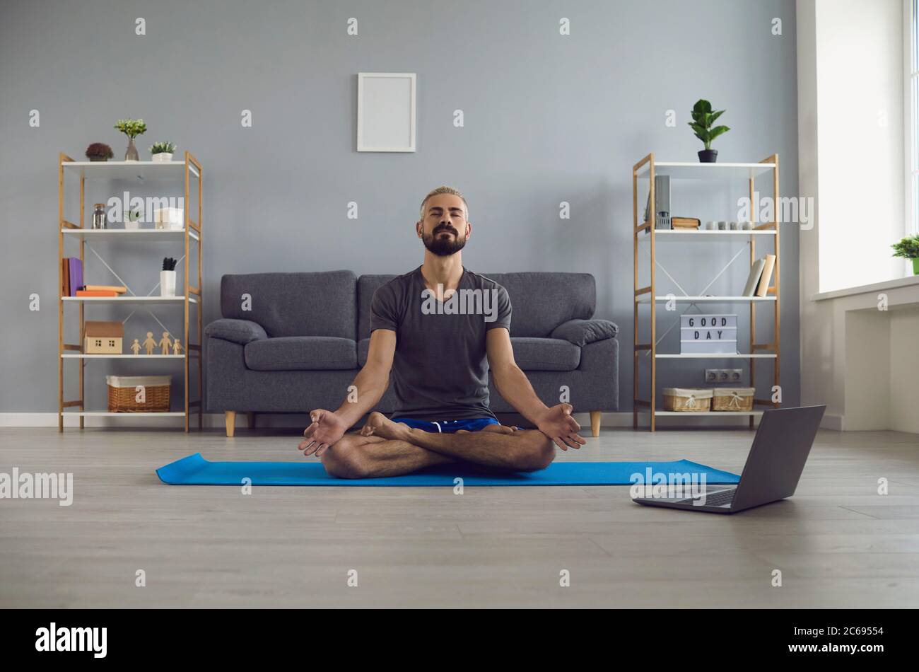 Lezione di yoga online. Giovane ragazzo tranquillo che pratica la meditazione mattutina di fronte al computer portatile a casa. Concetto di equilibrio di vita Foto Stock