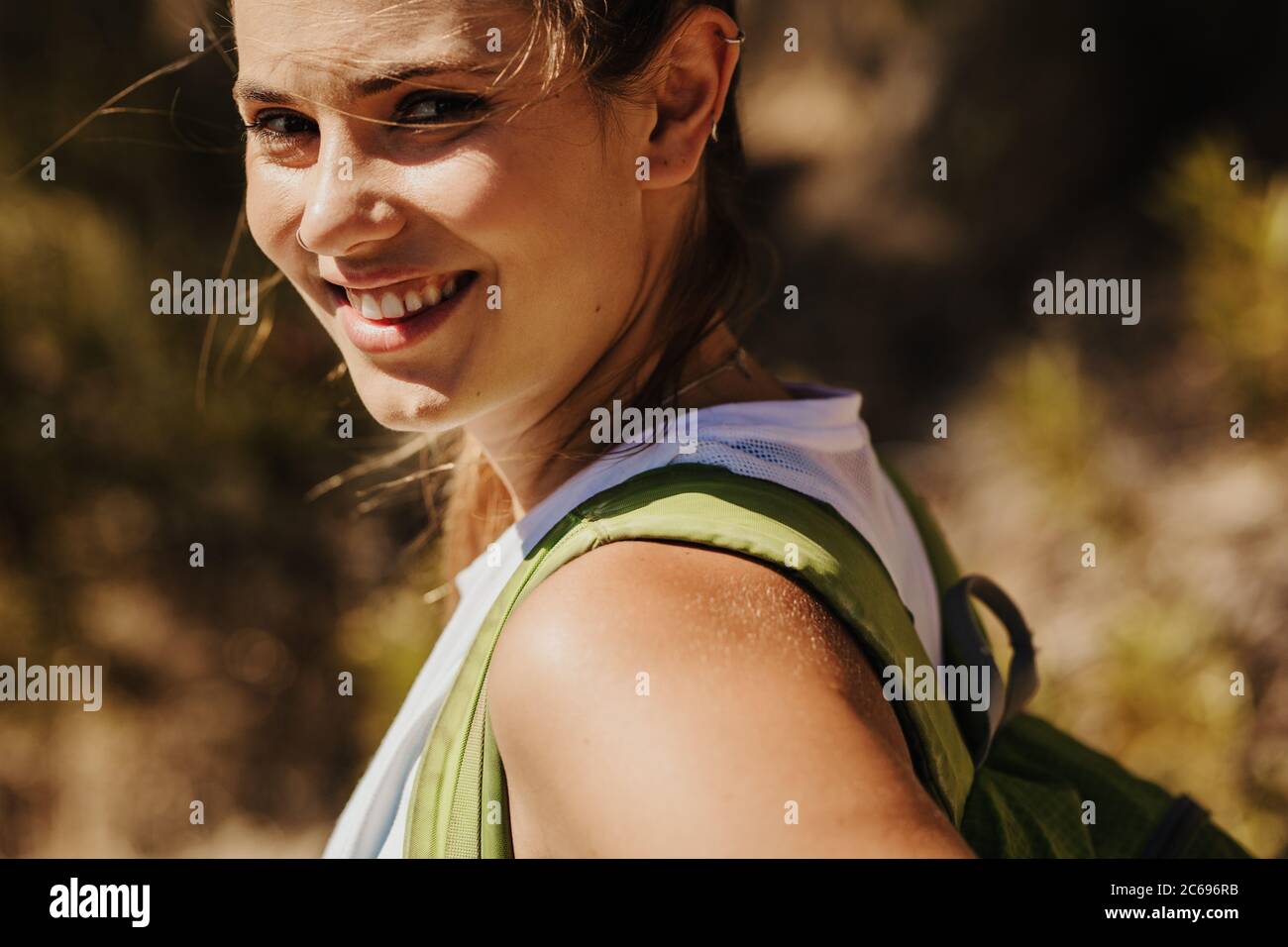 Primo piano di una bella donna trekking su un sentiero di montagna. Donna alpinista che sale una montagna guardando la macchina fotografica e sorridendo. Foto Stock