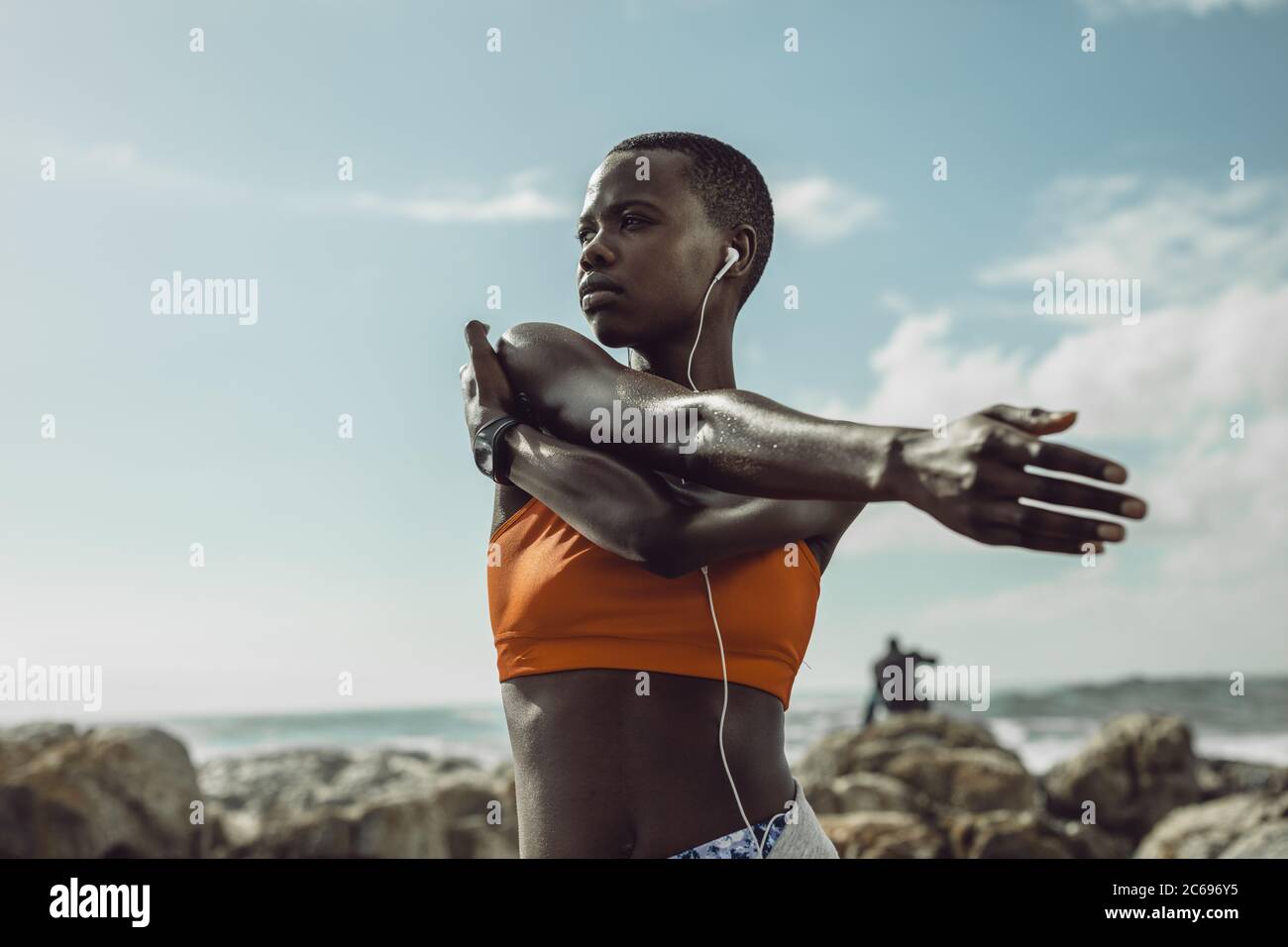 Donna africana con cuffie che allungano le braccia all'aperto. Donna in abbigliamento sportivo che si esercita in spiaggia. Foto Stock