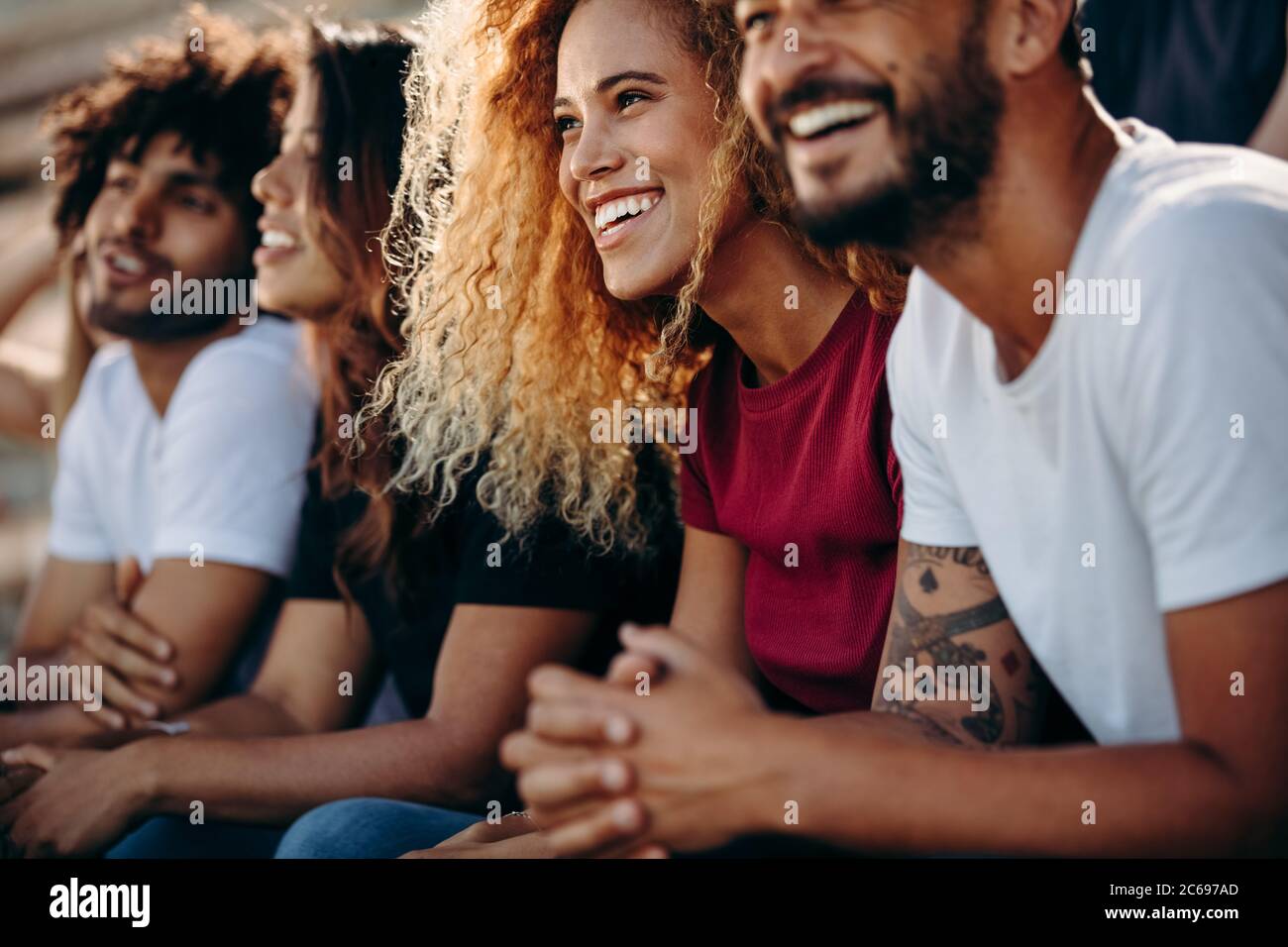 Giovane coppia che guarda un evento sportivo allo stadio. Gruppo multietnico di appassionati di sport che si siedono allo stadio e guardano una partita di calcio. Foto Stock
