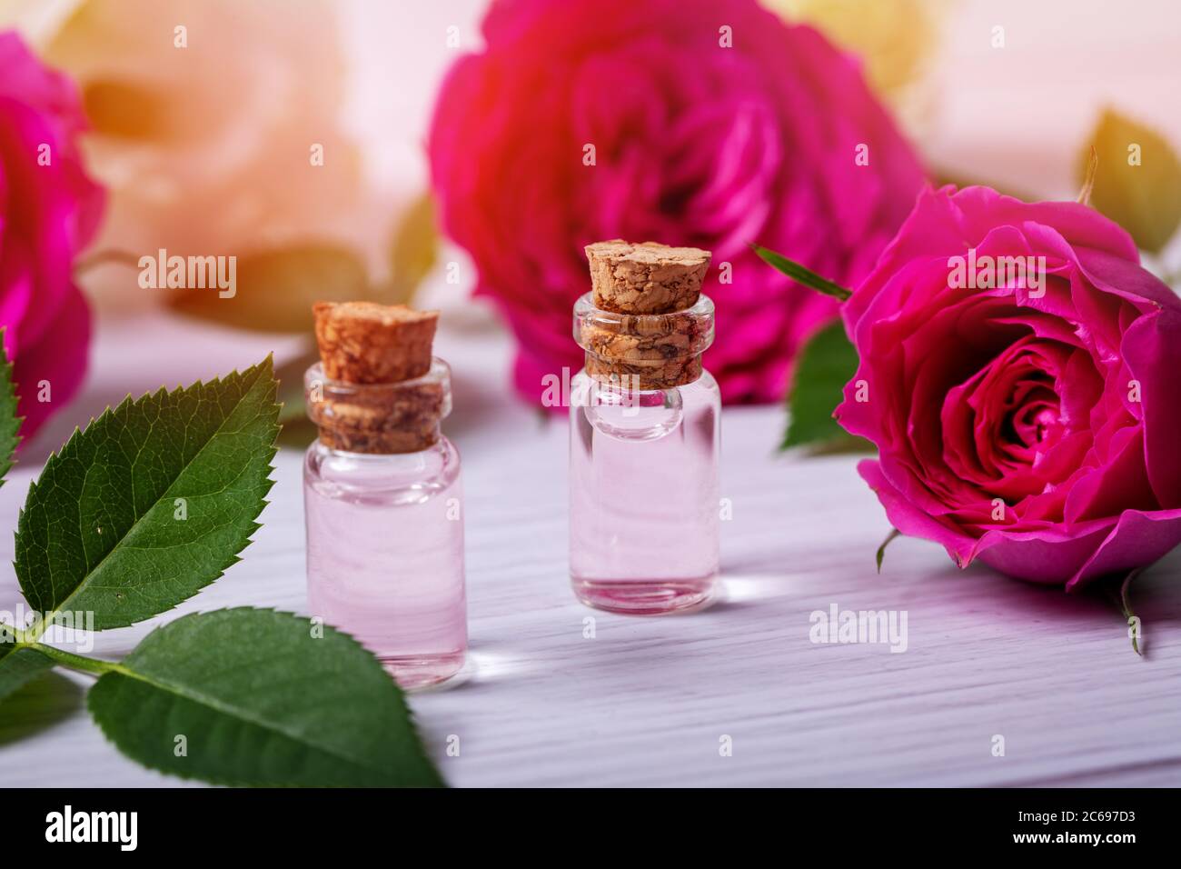 acqua di rosa profumata o olio essenziale in bottiglie di vetro con fiori su tavola di legno Foto Stock