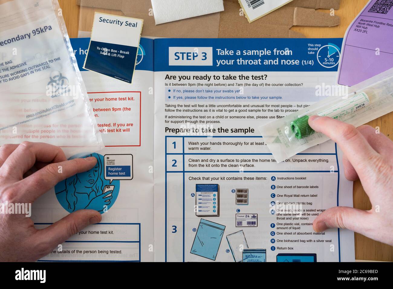 Il contenuto di un kit per test a domicilio di Coronavirus (Covid-19) si è distribuito su un tavolo con le mani di un uomo poggiate su un kit di campionamento e istruzioni Foto Stock