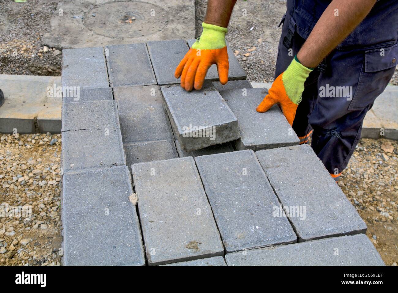 Il padrone sta mettendo i mattoni nuovi di calcestruzzo per il marciapiede sul palo. I mattoni sono stati preparati per la posa di un nuovo sentiero. Foto Stock