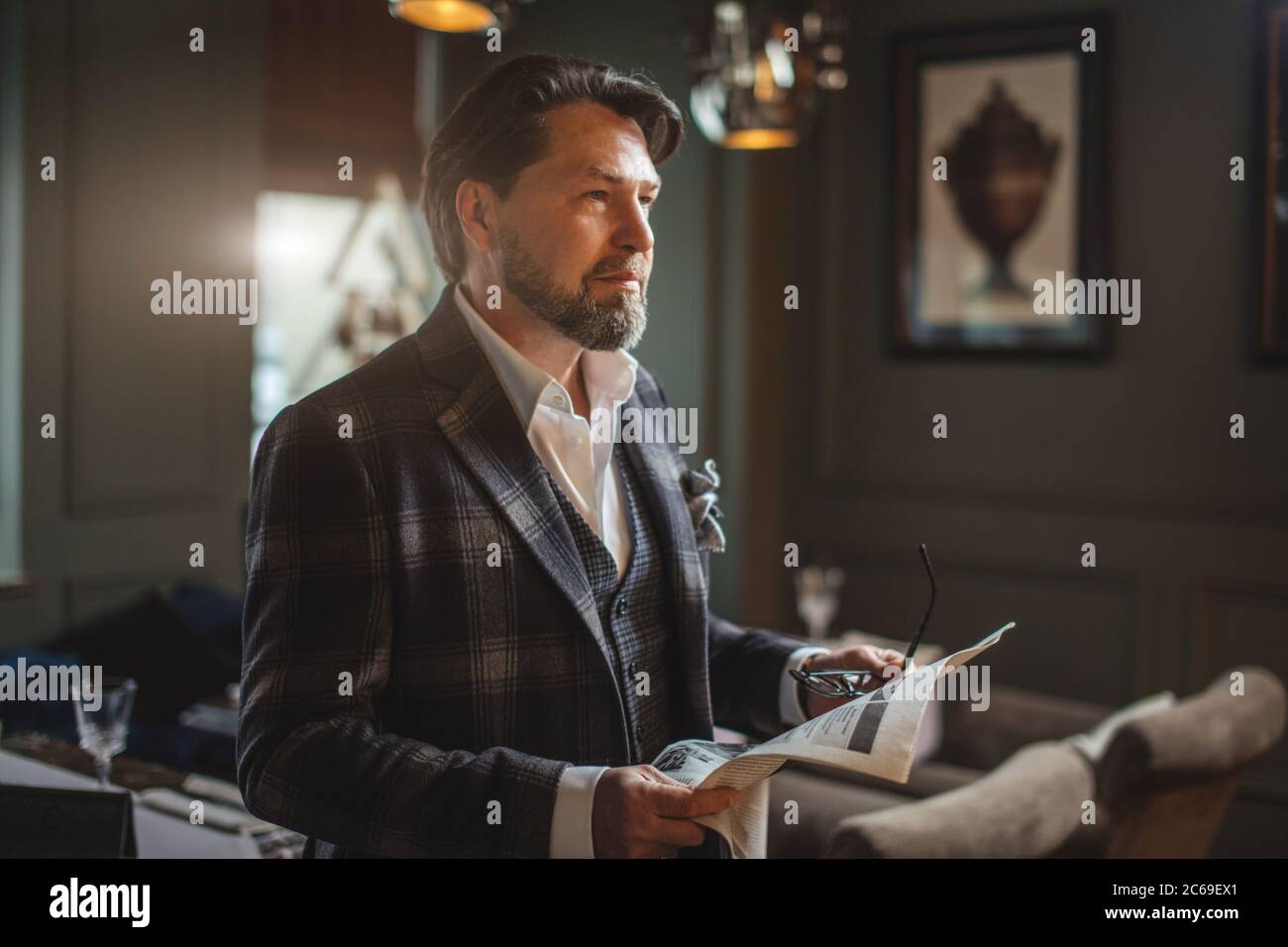 Fiducioso senior business man in eleganti custom made suit lettura quotidiano fresco mentre in piedi nel ristorante o bar Foto Stock