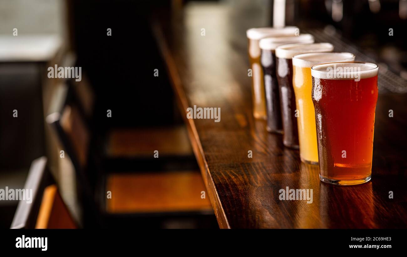 Festa con gli amici in pub. Fila di bicchieri di birra di vario genere sul bancone bar all'interno Foto Stock