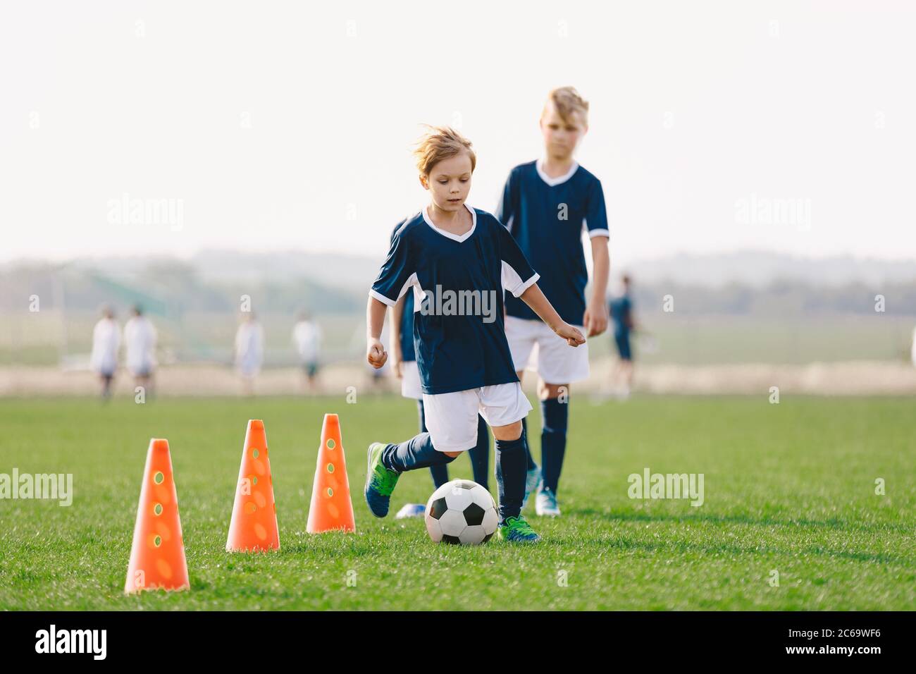 Unità di allenamento ragazzi sul campo da calcio. I giovani calciatori si  allenano con le abilità di dribbling sul campo da gioco. Bambini che  corrono tra coni di allenamento di calcio rossi.