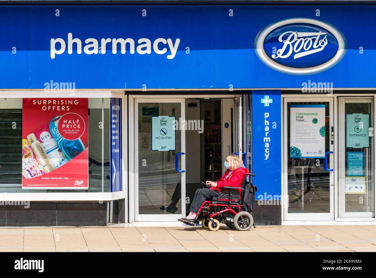 Edimburgo, Scozia, Regno Unito, 8 luglio 2020. Le maschere facciali sono la norma su Princes Street con sempre più persone che le indossano, soprattutto per andare nei negozi, anche se non diventano obbligatori nei negozi in Scozia fino a venerdì. Una donna anziana in una sedia a rotelle elettrica che indossa una maschera che passa davanti all'ingresso del negozio di articoli chimici Foto Stock