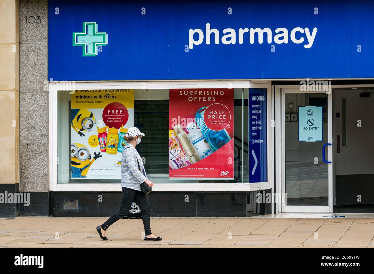 Edimburgo, Scozia, Regno Unito, 8 luglio 2020. Le maschere facciali sono la norma su Princes Street con sempre più persone che le indossano, soprattutto per andare nei negozi, anche se non diventano obbligatori nei negozi in Scozia fino a venerdì. Una giovane donna che indossa una maschera cammina oltre gli stivali del negozio chimico Foto Stock