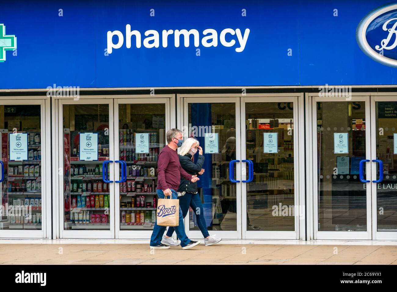 Edimburgo, Scozia, Regno Unito, 8 luglio 2020. Le maschere facciali sono la norma su Princes Street con sempre più persone che le indossano, soprattutto per andare nei negozi, anche se non diventano obbligatori nei negozi in Scozia fino a venerdì. Una coppia che indossa maschere facciali con una borsa per lo shopping di Boots farmacia che passa accanto a Boots il negozio di farmacia Foto Stock