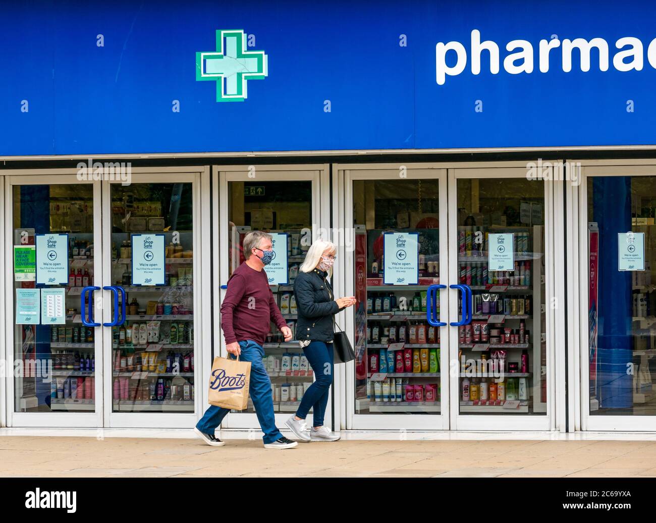 Edimburgo, Scozia, Regno Unito, 8 luglio 2020. Le maschere facciali sono la norma su Princes Street con sempre più persone che le indossano, soprattutto per andare nei negozi, anche se non diventano obbligatori nei negozi in Scozia fino a venerdì. Una coppia che indossa maschere facciali con una borsa per lo shopping di Boots farmacia che passa accanto a Boots il negozio di farmacia Foto Stock
