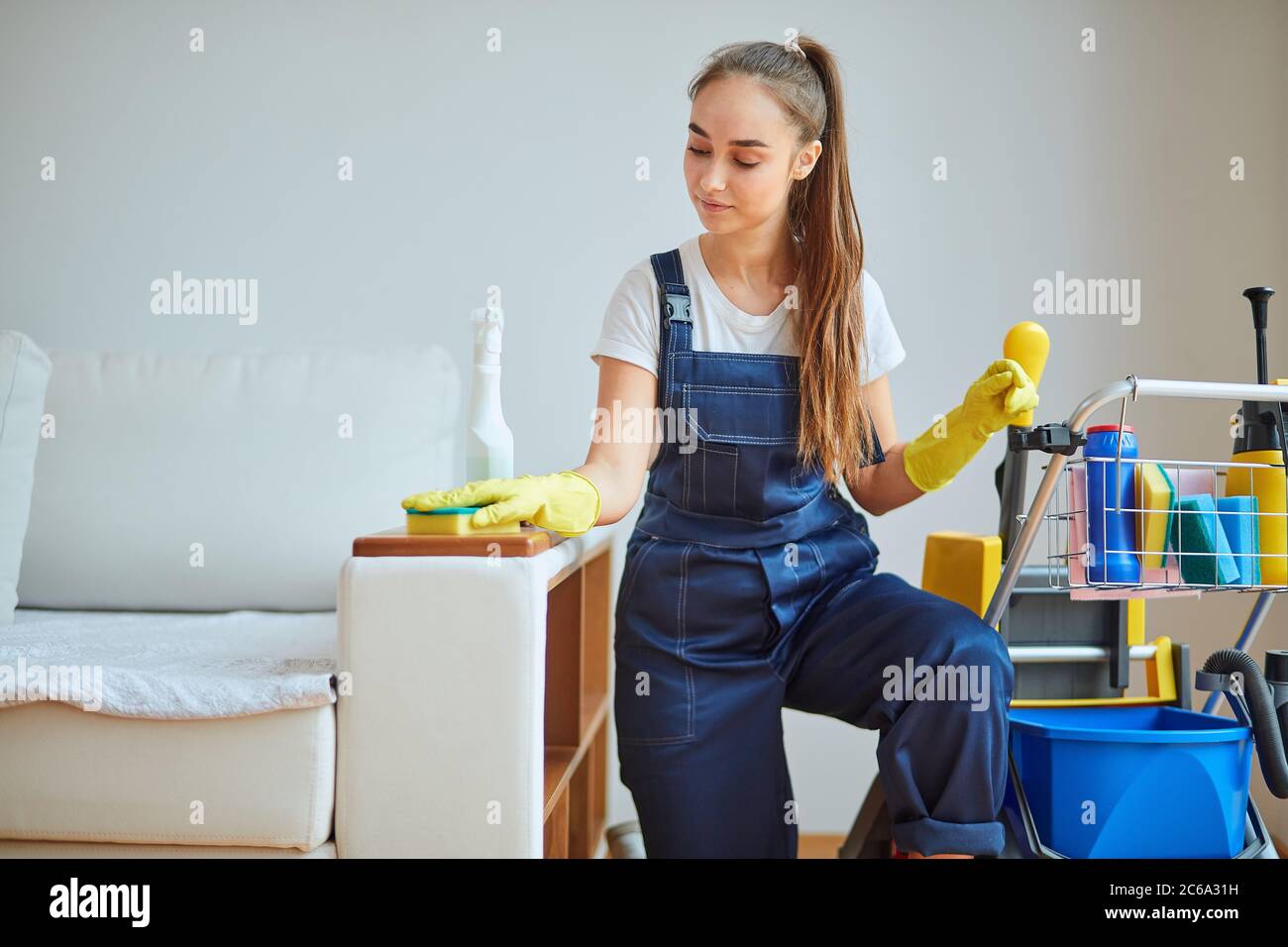 Personale giovane della camera di pulizia. Bella ragazza che indossa attrezzatura speciale con guanti di gomma gialla, utilizzando spray per rimuovere la polvere. Attento lavoratore di pulito Foto Stock