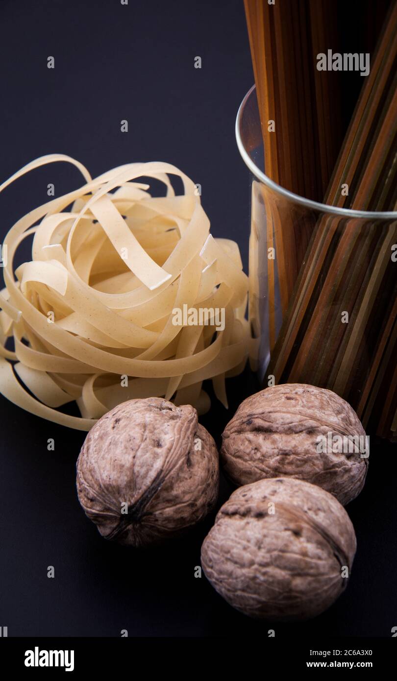 Pasta lunga marrone e pasta sagomata accanto a un certo numero di noci da vicino. Foto Stock