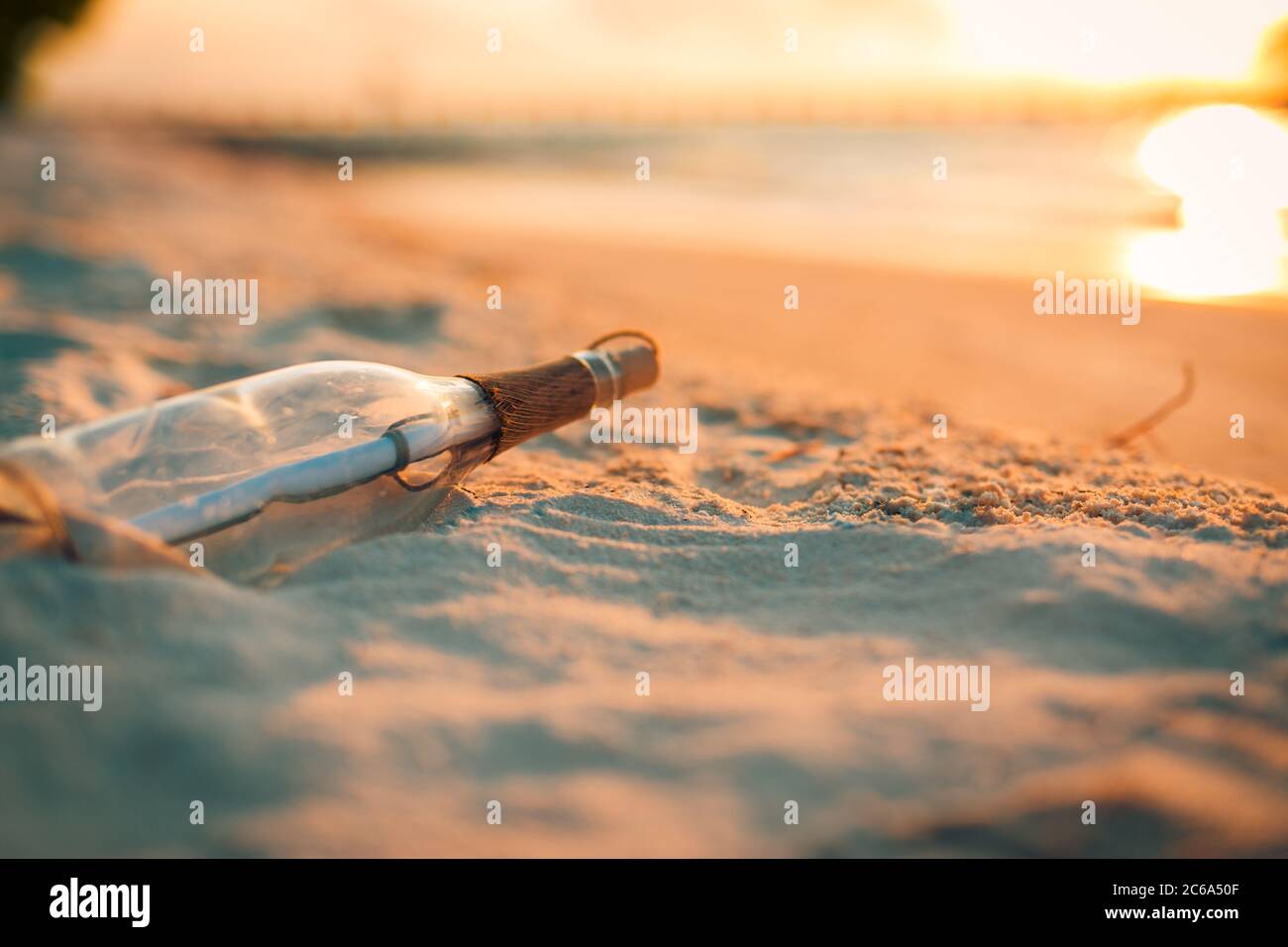 Tramonto tropicale, messaggio in una bottiglia concetto. Messaggio in bottiglia lavato a terra contro il tramonto. Sfondo di design tropicale della spiaggia Foto Stock