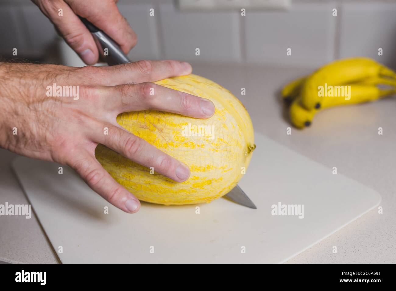L'uomo al tavolo da cucina taglia il melone maturo Foto Stock