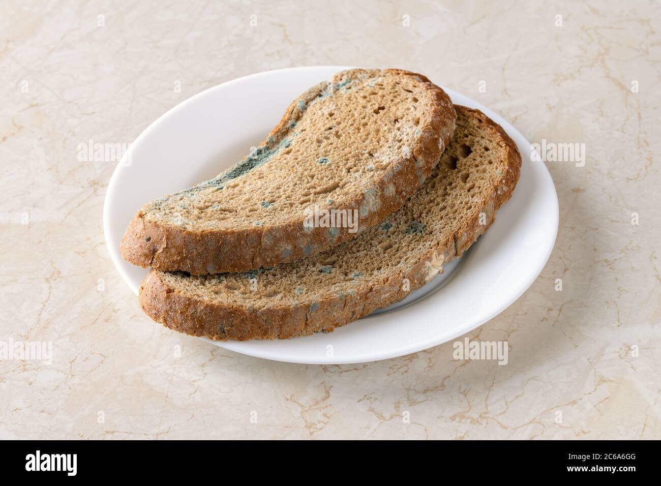 Due fette di pane di segale con muffa verde su un piatto bianco sopra il tavolo da cucina. Fungo ammuffito su pane marcio. Pane guastato con muffa. Vista frontale Foto Stock