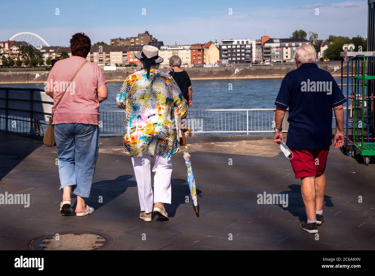 Donna in blusa colorata con cappello e ombrello cammina con i compagni attraverso il porto di Rheinau, Colonia, Germania Frau in bunter Bluse mit Hut und Re Foto Stock