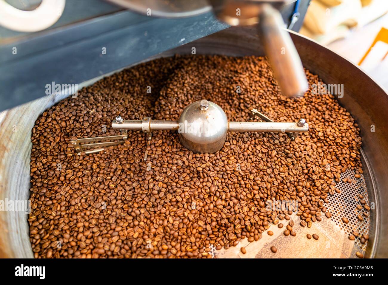 Chicchi di caffè appena tostati da un grande arrosto nel cilindro di raffreddamento. Sfocatura del movimento sui chicchi. Foto Stock