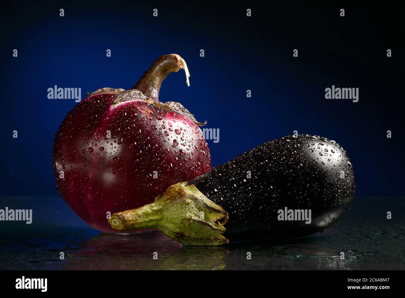 Due melanzane con gocce d'acqua su sfondo blu scuro o nero, sparate nello Studio Foto Stock