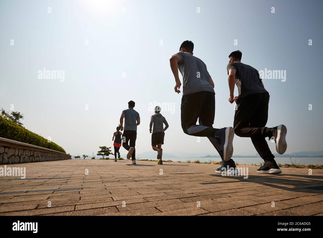 gruppo di giovani adulti asiatici che corrono all'aperto, con vista posteriore e ad angolo basso Foto Stock