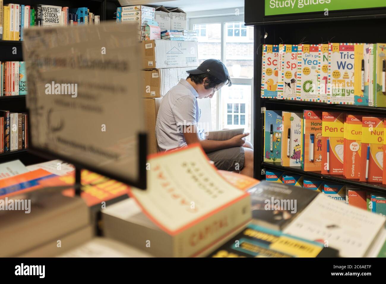 Ragazzo adolescente, 13-14 anni legge un libro in libreria, Londra, Regno Unito Foto Stock