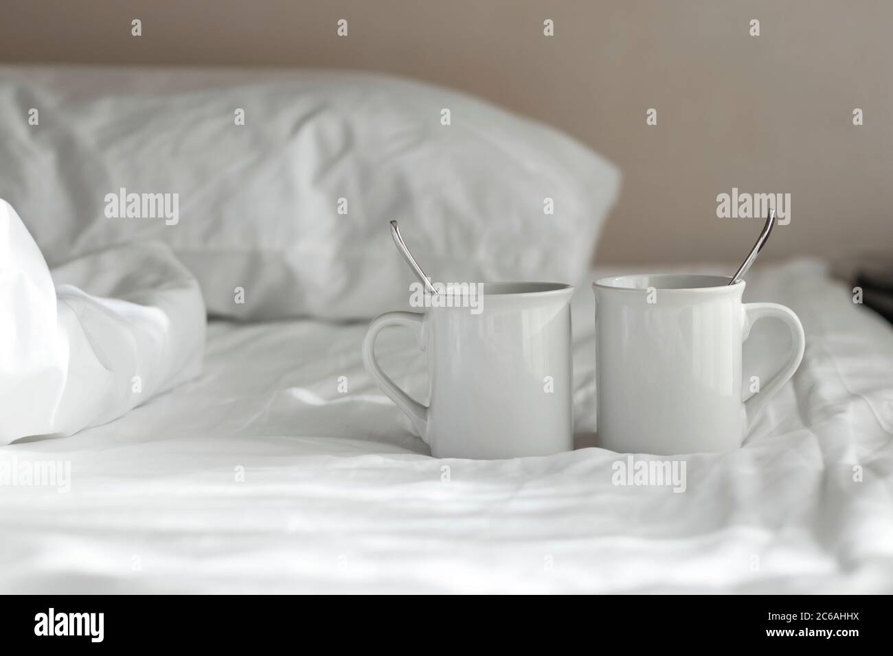 Due tazze bianche con cucchiaio si stese sul letto al mattino. Foto Stock